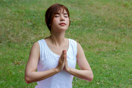 Young asian woman in sportswear meditating while sitting in lotus pose on yoga matの写真素材
