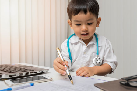 little boy in medic uniform using a pen on deskの写真素材