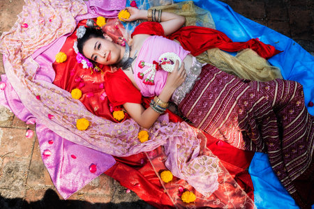 Beautiful Thai woman wearing thai traditional clothing lie down on silk of various colors.