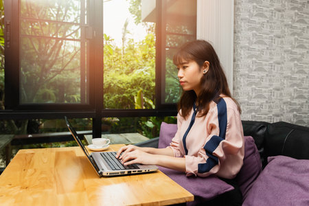 Beautiful young Asian woman using laptop computer while sitting in a vintage coffee shopの写真素材