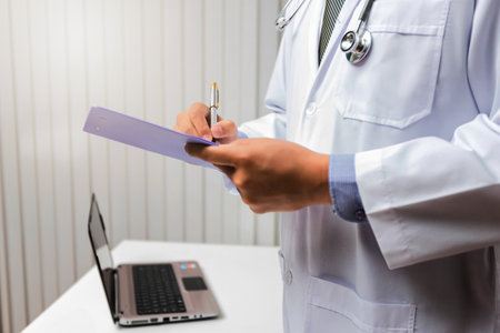 Doctor in gown uniform using a pen write on medical chartの写真素材