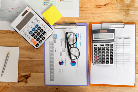 Top view of business paper chart or graph with glasses and calculator on wooden table. Wooden office desk with office supplies.の写真素材