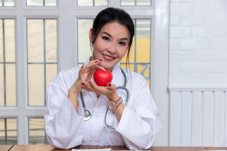 Female doctor holding a red heart ball in the hospital. Concept of health care and medical.の写真素材