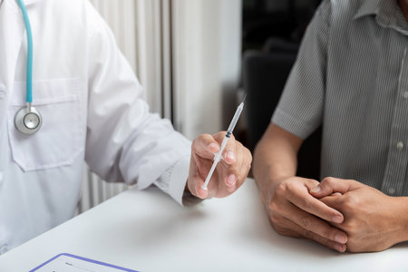 Medical, medicine, vaccination and health care concept. Doctor with syringe doing injection of vaccine to male patient while sitting at the table in office.の写真素材