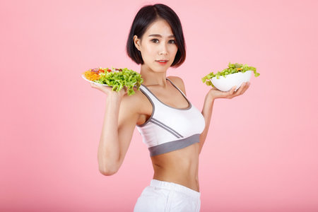 Beautiful young healthy woman with salad bowl isolated over pink background. Fitness Diet and healthy eating concept.の写真素材