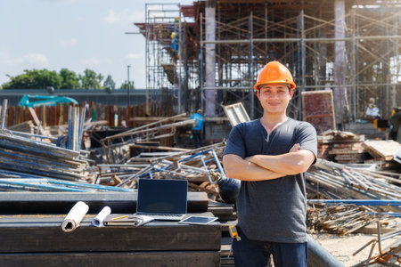 Male Engineer with arms crossed standing at a construction site looking happy.