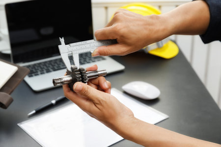 The engineering team is working on their project together. Man work with caliper measure the motor gear, engine part.の写真素材