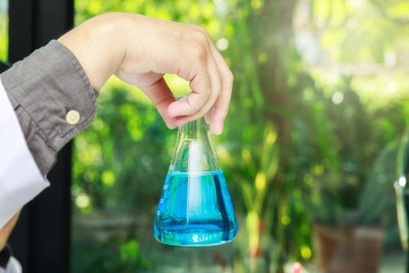 Beaker with blue experiment liquid in scientist hand on laboratory background, science concept.の写真素材