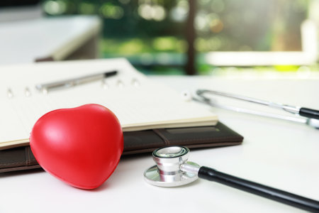 Red heart ball and stethoscope on a white wooden table.の写真素材