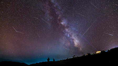 Long time exposure night landscape with the milky way during meteor shower over a mountain with hut.