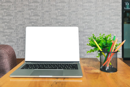 Laptop with blank screen, pencils, vase on table in home office. Workspace with laptop and office supplies.の写真素材