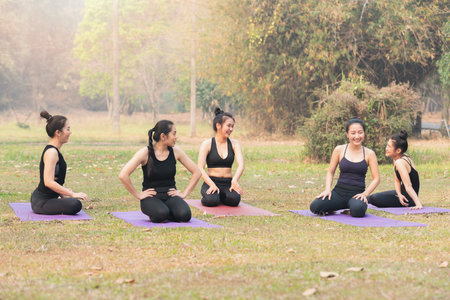 Group of asian women having rest after practices yoga. Women sitting and talking in outdoor park.の写真素材