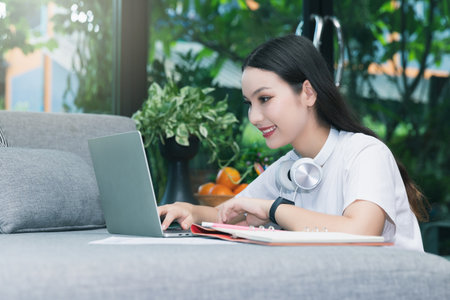 Beautiful asian woman smiling and looking at laptop in living room. Working, Learning from home...