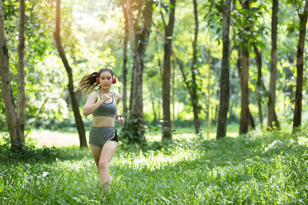 Young woman runner listening music on headphones while running on tropical rainforest trail in the morning.の写真素材