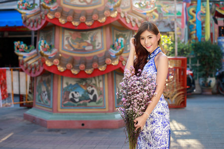 Chinese woman in cheongsam dress with a bouquet of flowers at shrine. Concept to celebrate Chinese...