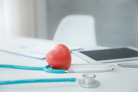 Red heart ball with stethoscope and digital tablet on a white wooden table.
