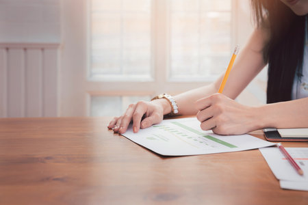 Close up of asian woman hand holding pencil analysis the graph at the home office for setting challenging business goals And planning to achieve the new target.の写真素材