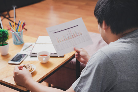 A man in casual wear picks up cookies while he is working at home office.の写真素材