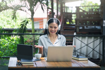 Beautiful young asian woman with headphone on online video call via laptop at the outdoor cafe. Online conference with laptop.の写真素材