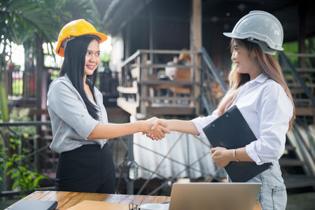 Two asian female architect and engineer in protective helmets shaking hands after meeting. Success collaboration concept.の写真素材