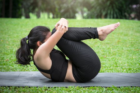 Asian woman doing yoga poses to strengthen lower back and core body on mat in outdoor park.の写真素材