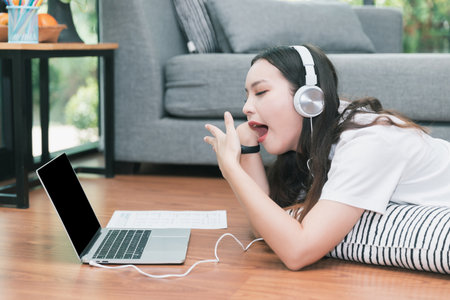 Young asian woman with headphone open mouth yawning while lying on the floor in living room....