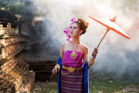 Beautiful Thai woman wearing thai traditional clothing with red umbrella in amid the smoke and fog.の写真素材