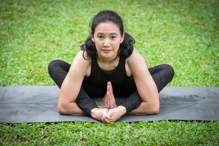 Asian woman practicing yoga on mat in outdoor park.の写真素材