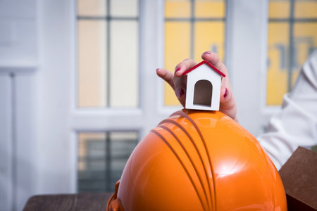 Female real estate agent presenting a house model. Young female architect holding model of house in...