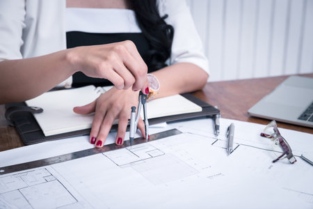 Female architect using dividers working on blueprint architects project in office.の写真素材