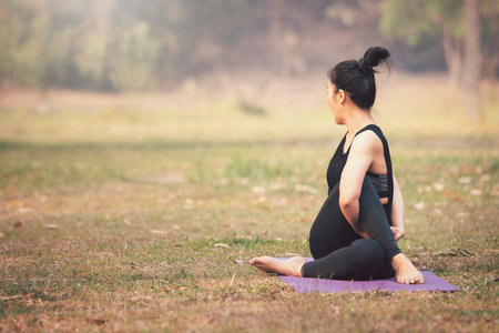 Asian woman practicing yoga on mat in outdoor park.