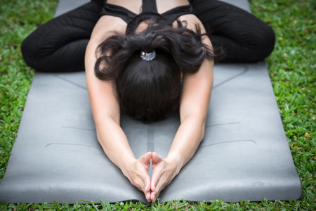 Asian woman practicing yoga in child with fire log pose or seated forward bend on the mat in outdoor park.の写真素材