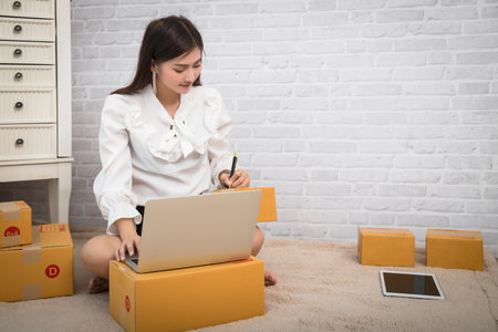 Successful entrepreneur business woman using laptop to check and prepare parcel box of product for...