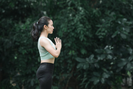 Asian woman practicing yoga in Tree poses, Vrikshasana on the mat in outdoor park.