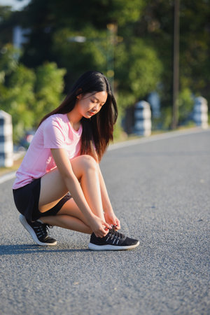 Close up of female runner kneeling and tying shoelace on the street. Fitness woman tying shoelaces. Young woman runner tying shoelaces in park with sunset and sunbeam.の写真素材