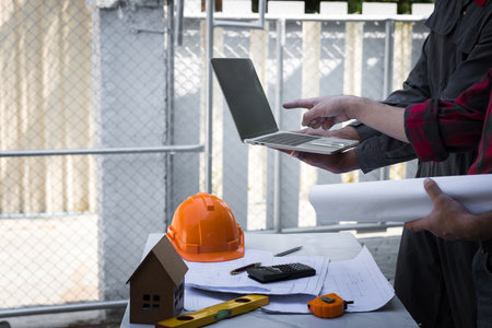 Engineers and architects pointing at laptop screens looking at blueprints. Two Construction Engineers or Architects discussing at work with laptop on construction site and pointing on laptop.の写真素材