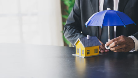 Man holding wooden umbrella and house. An insurance agent is holding a blue umbrella over a modern house model. Property insurance concept. home and real estate insurance concepts.の写真素材