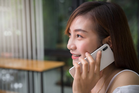 Head shot smiling asian woman holding mobile phone talk with friend. Close up Young Office Woman Talking on Mobile Phone. Close up head shot young woman holding smartphone, talking, phone call.の写真素材