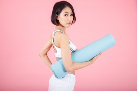 Portrait of woman holding exercise mat roll, holding yoga mat roll on pastel pink background.の写真素材