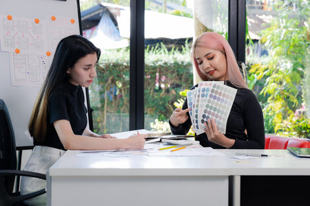 Women holding and point to a color chart for home design. Graphic designers working on color chart at modern office.の写真素材