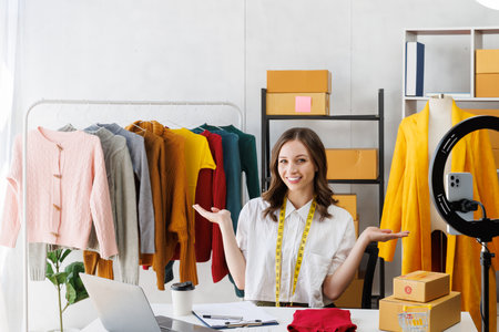 Beautiful woman describe selling clothes on camera live broadcast on social network at home, Online selling clothes on social media. Vlogger woman influencer, SME retail store owner.の写真素材