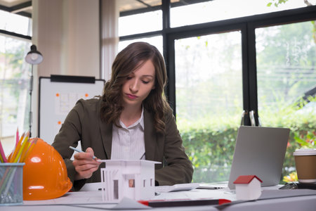 An architect woman or engineer woman working on blueprint with model house in office, architectural concept.の写真素材
