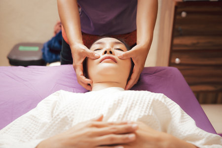 woman in spa gets facial and head massage in a beauty clinic. Close-up of young woman getting spa massage treatment at beauty spa salon. Spa skin and body care. Facial and head beauty treatment.の写真素材
