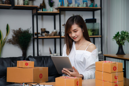 Successful entrepreneur business woman using laptop to check and prepare parcel box of product for delivery to customer . Woman with online sales and Parcel shipment in her home office.の写真素材