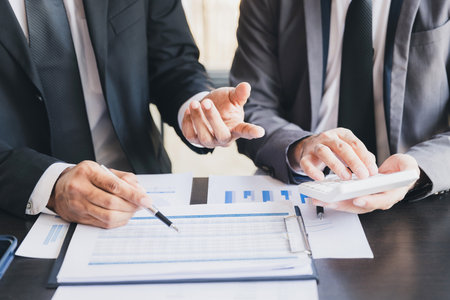 Two Businessman bsing calculator calculating data in reports and Financial data analyzing. Business team meeting and discussing project plan. Businessmen discussing together in meeting room.の写真素材