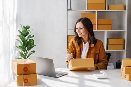 Business owner writing customer address on parcel boxes to deliver products to customers at home. Woman writing address on cardboard box at workplace. Small business entrepreneur SME.の写真素材