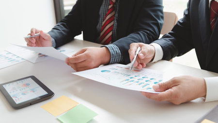 Close-up of two businessmen with pens pointing on report paper. Business team presentation meeting Asian Men Finance Executive discusses meetings to plan work, investment projects.の写真素材