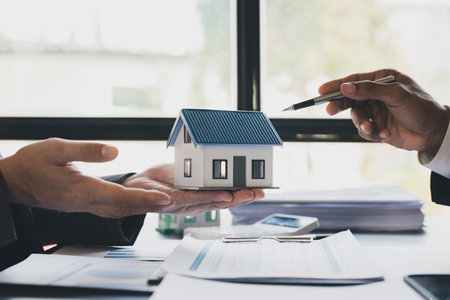 Real estate agent home sales broker holding calculator and pointing to the house model and explains the business contract, rent, buy, mortgage, loan or home insurance.の写真素材