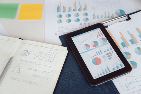 Workplace desk top angle view report on digital tablet with paper documents reports finance graph...
