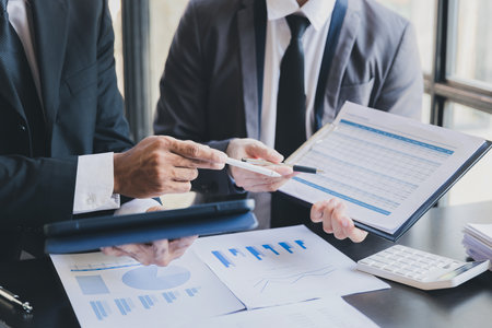 Close-up of two businessmen with pens pointing on report paper. Business team presentation meeting Asian Men Finance Executive discusses meetings to plan work, investment projects.の写真素材